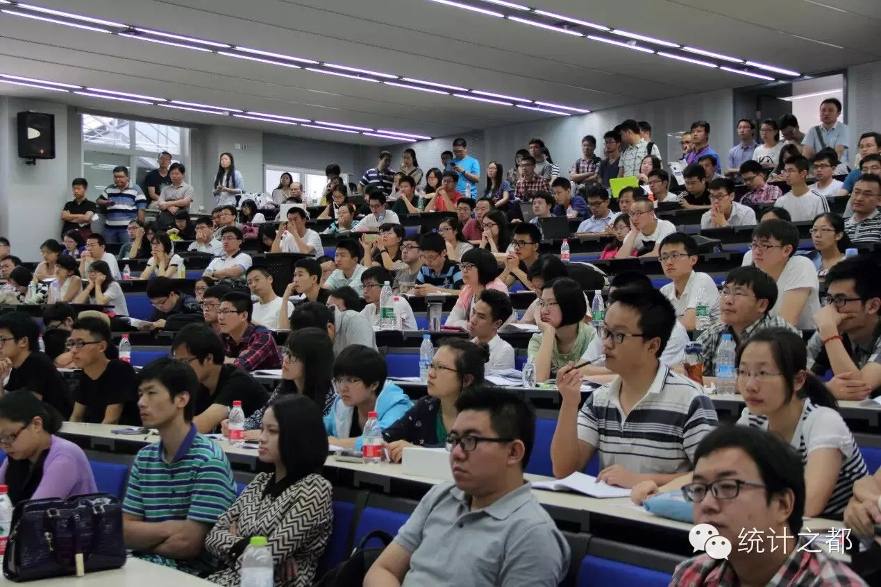 阶梯教室内坐满参会者，前排与后排听众面向讲台认真听讲。