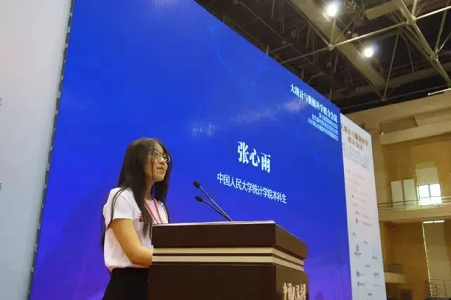 一名发言者站在大型蓝色会议屏幕旁的讲台上致辞。