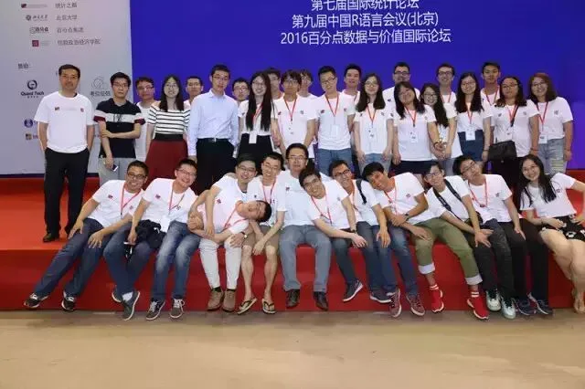 一群身穿白色会务衫的组织人员在会议背景板前合影。