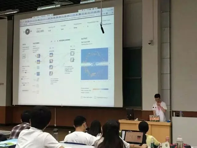 分会场内，演讲者在投影屏幕前操作电脑，听众从座位上观看。