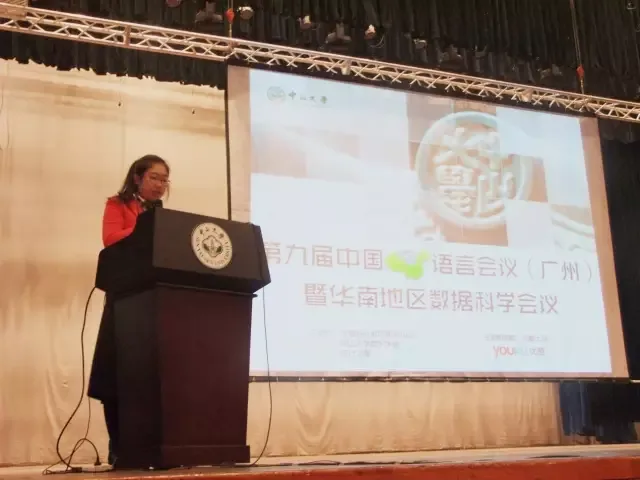 一名发言者站在讲台前，身后投影着第九届广州会议画面。