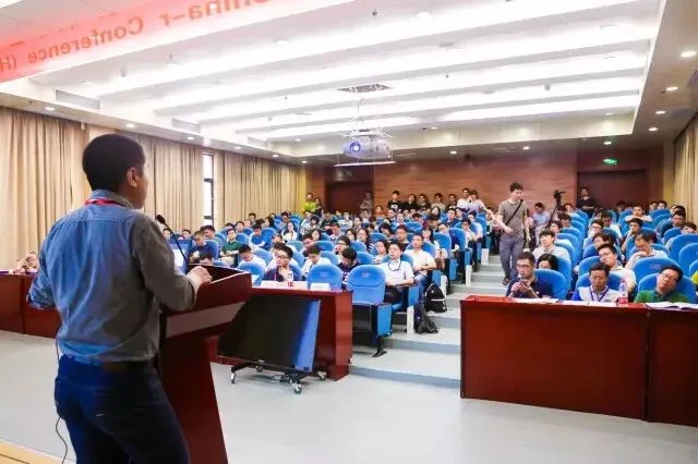 演讲者从讲台前面向坐满听众的报告厅发言。