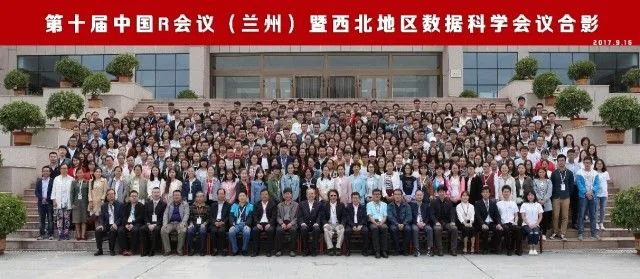 数百名参会者在教学楼前和红色会议横幅下拍摄集体照。