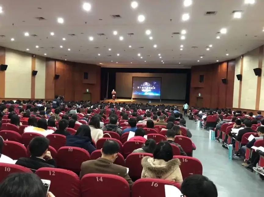 从后排望向报告厅，红色座椅中的大批听众面向远处舞台。