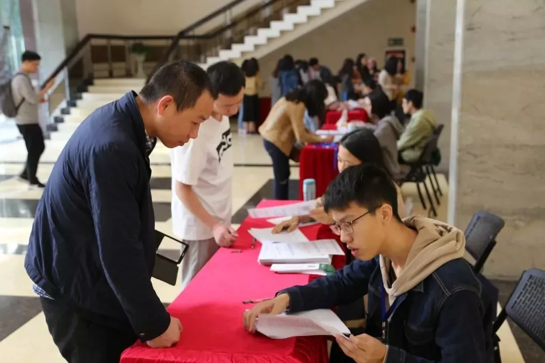 会场入口处，志愿者在红色签到桌后为一名参会者办理登记。