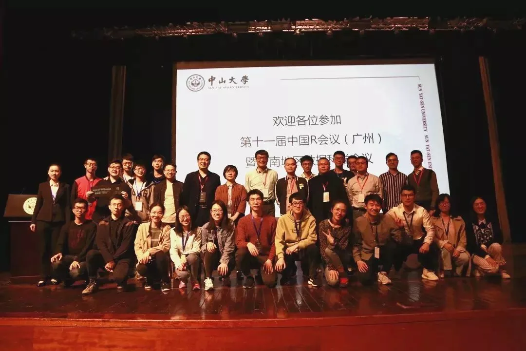 数十名参与者在舞台投影屏幕前站成两排拍摄合影。