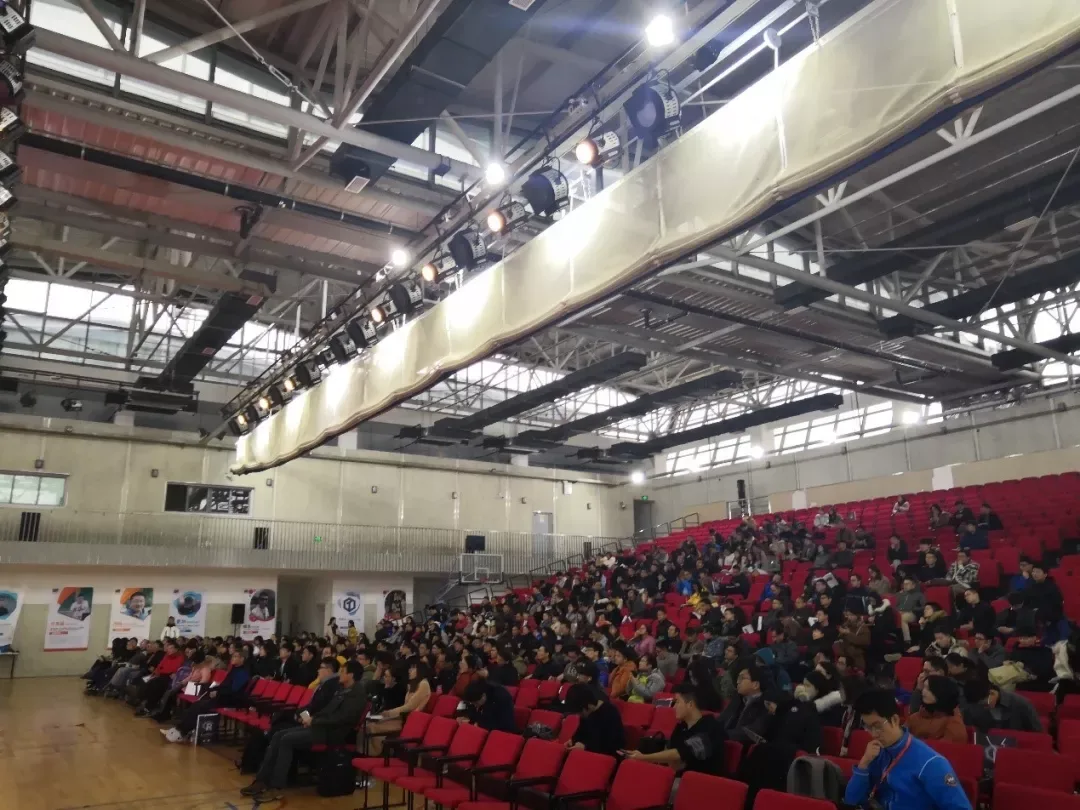 体育馆内布置了大面积红色座席，参会者面向场地中央的主舞台。