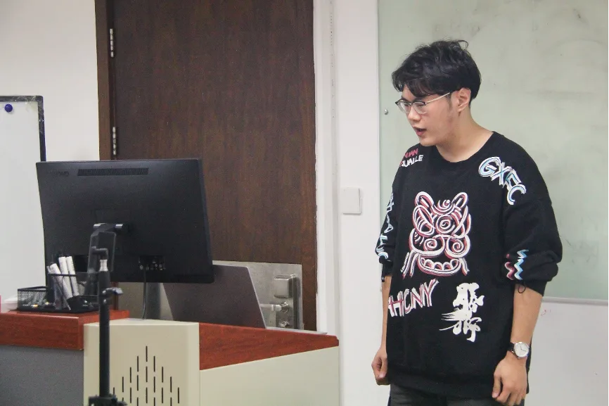 一名演讲者站在教室前方的显示器和讲台旁发言。