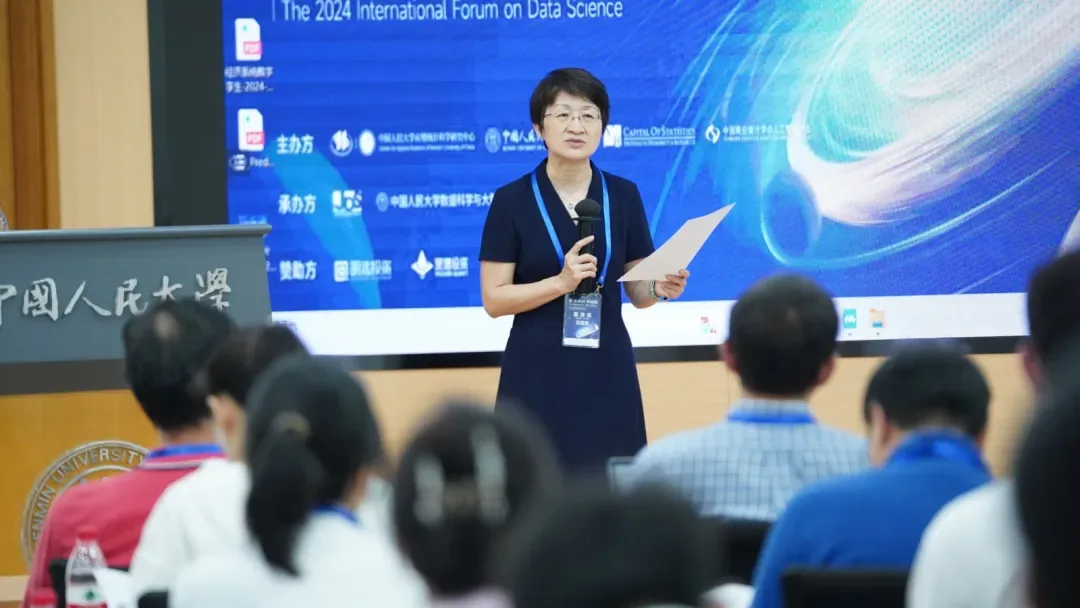 一名发言者手持话筒站在蓝色数据科学国际论坛背景屏幕前，前景为就座听众。