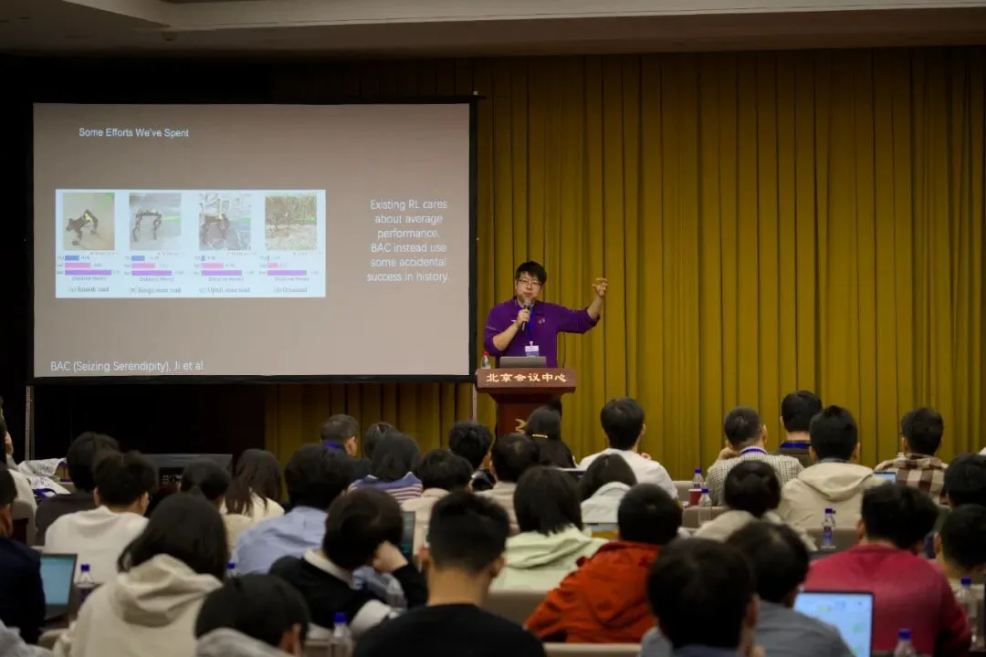 从后排望向坐满听众的会场，一名演讲者在北京会议中心讲台前展示报告幻灯片。
